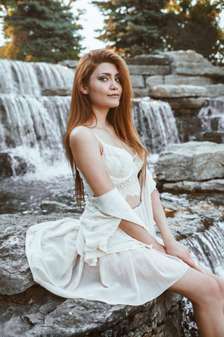 CharmaineLouise Books CLBooks Sexy pretty Dominatrix sub switch woman with long red hair wearing white lace bustier under unbuttoned short white dress sitting by waterfall